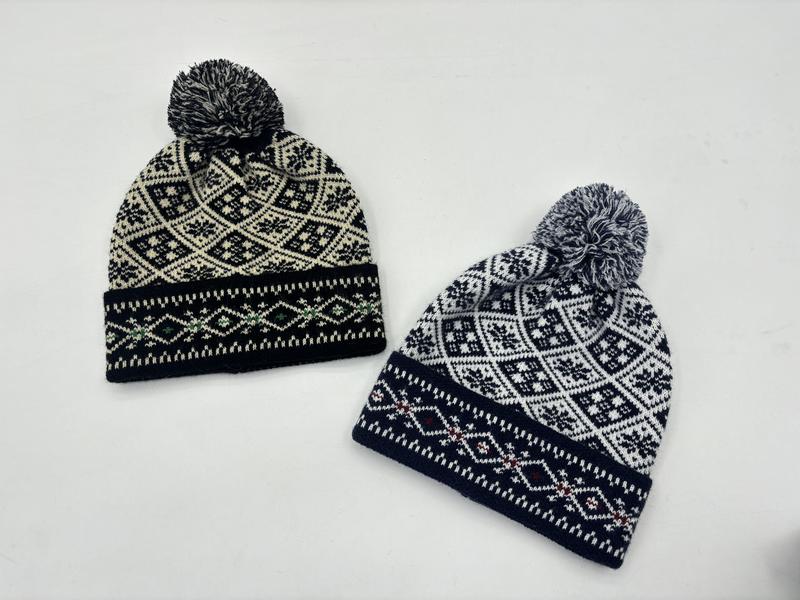 ""Två Fair Isle-mössor med pom pom i svart/vit och marinblå/vit nordisk snöflingmönster mot vit bakgrund.""