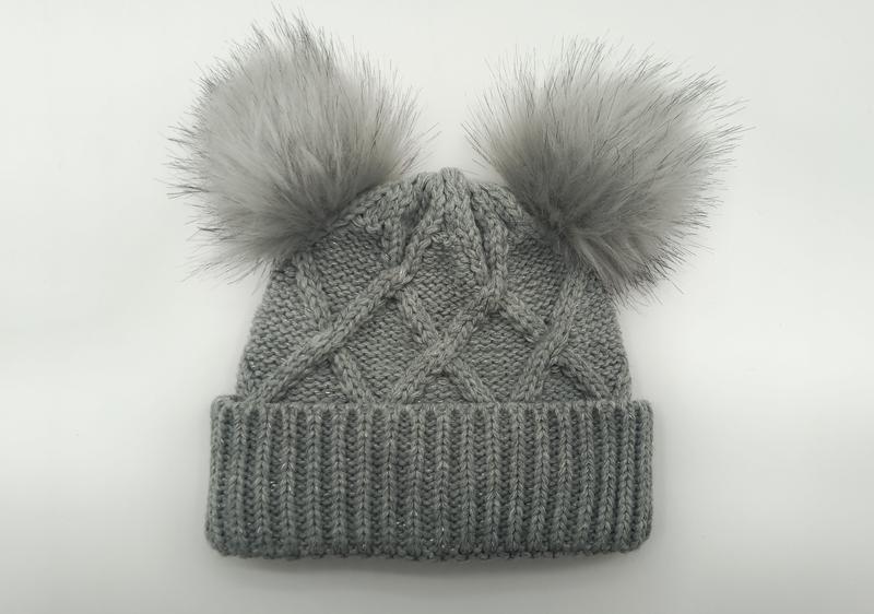 Grå kabelstickad vintermössa med dubbla fluffiga pom poms i konstpäls
