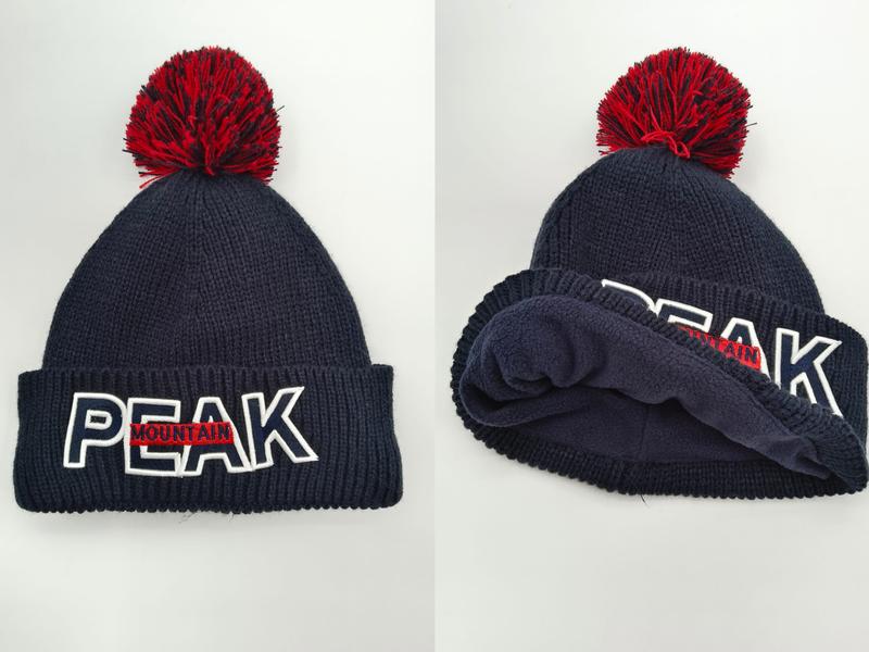 Marinblå ribbstickad mössa med röd pompom och broderad PEAK MOUNTAIN-logga på uppvikt kant