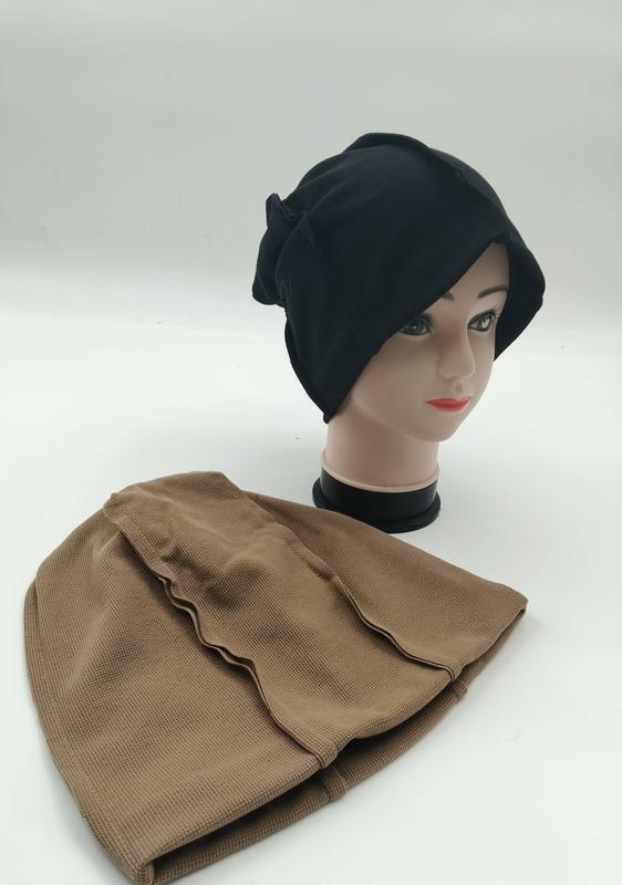 Svart slouchy beanie hijab underscarf på mannekänghuvud med beige texturerad inre mössa bredvid.