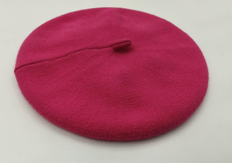 Platt bild av en het rosa stickad ullbasker med ribbad kant och mittknapp mot vit bakgrund.