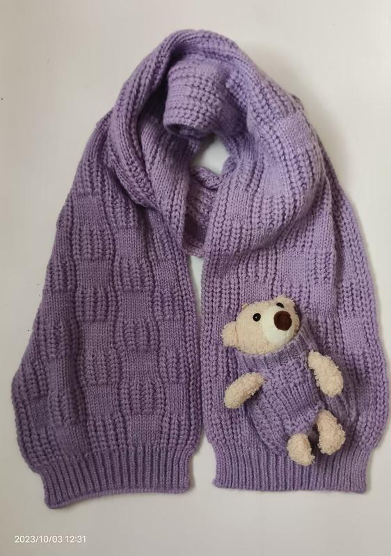 Lavendelfärgad grovstickad halsduk med krämbjörn i ficka – grossistleverantör av trendiga accessoarer.