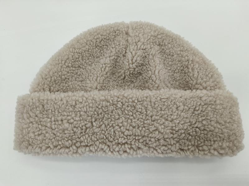 `Beige sherpa-mössa med lockig fleecetextur och uppvikta kanter för varm vinterstil.`