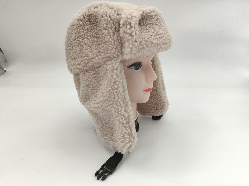 Krämvit lockig sherpa fleece trapperhatt med öronlappар och fäste under hakan.