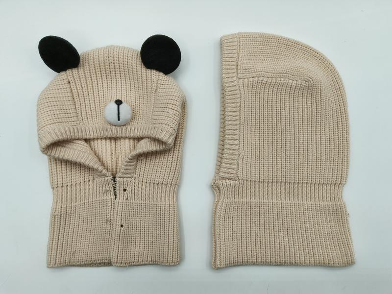 Beige stickad björnbalaclava med svarta öron och broderat ansikte.