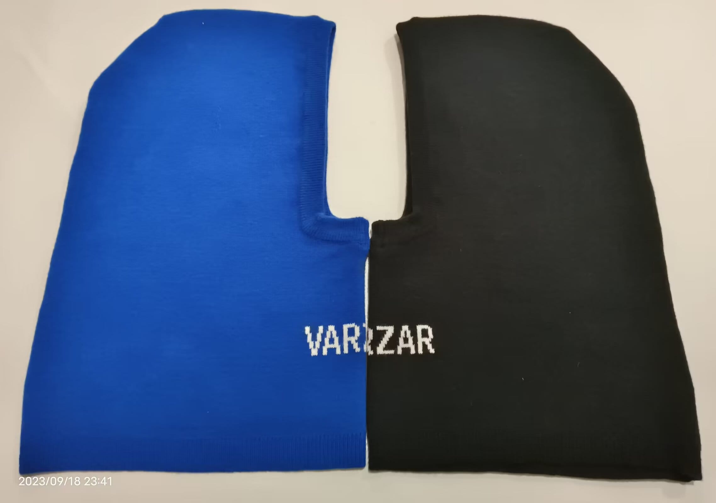 Blå och svart stickad balaclava i två färger med ansiktsöppning och varumärkeslogotyp – grossistleverantör.