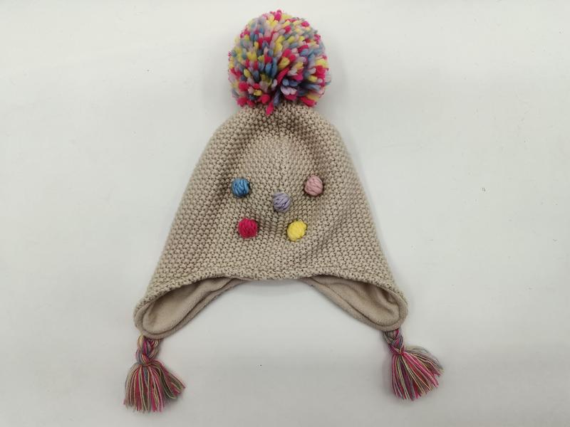 Beige stickad vintermössa för barn med färgglad pompom och tofsar.