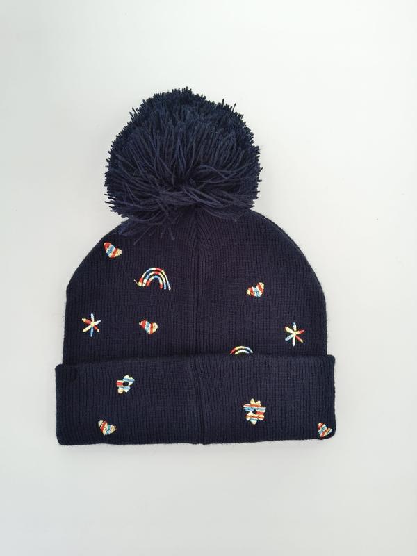 Marinblå ribbstickad vintermössa med stor pompom och färgglada broderade regnbågar