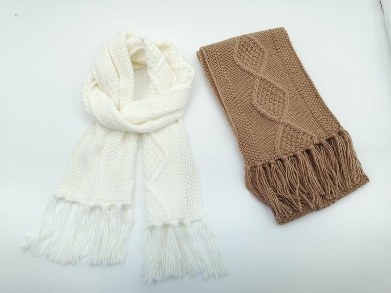 `Två kabelstickade halsdukar med fransar: en crèmefärgad oändligshalsdukar och en vikt kamelbeige.`