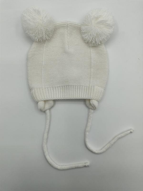 Vit stickad babymössa med två fluffiga pompomer och knytband under hakan