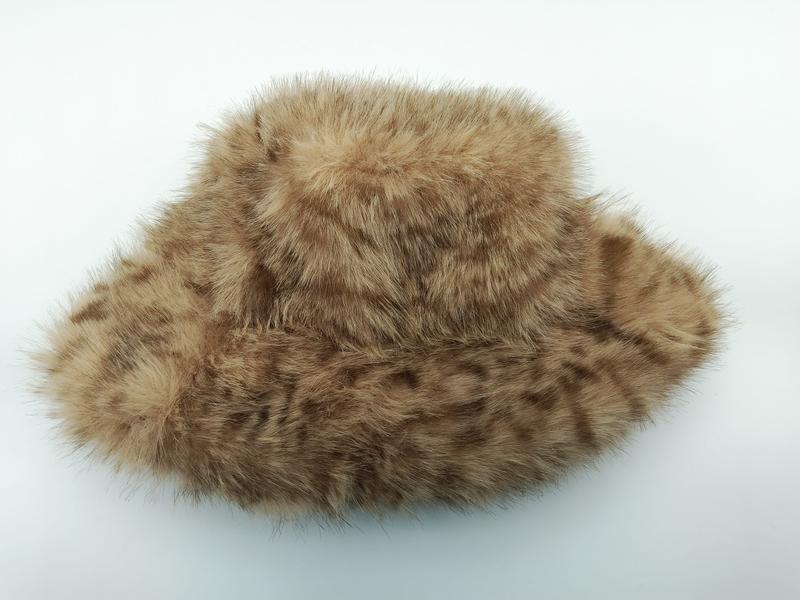 Brun och beige prickig fejkpälsbuckethat med bred brätte och fluffig textur på vit bakgrund.