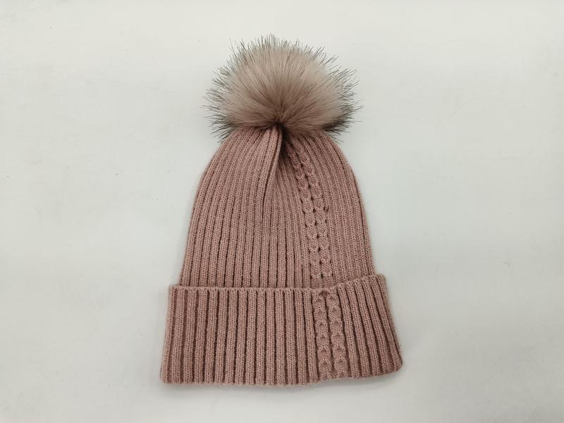 Rosa ribbstickad vintermössa med stort konstpälspom-pom mot vit bakgrund.