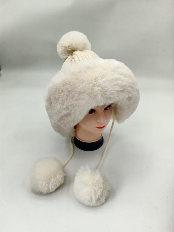 Krämvit konstpälsmössa med stickad pompom och hängande pälspomponger på snörena.