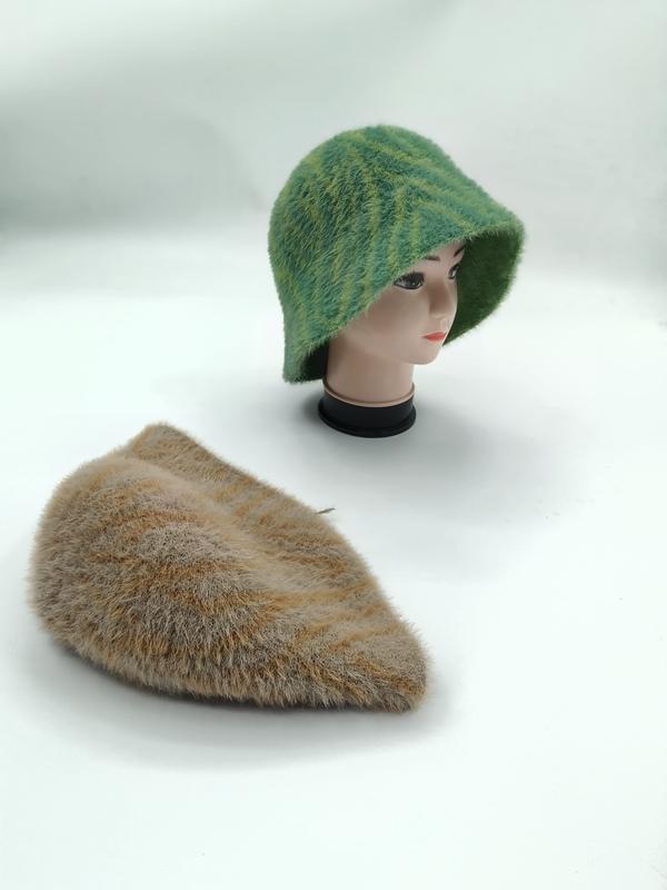 Grön randig fluffig stickad bucket hat på skyltdockshuvud med matchande beige flat cap på vit yta.