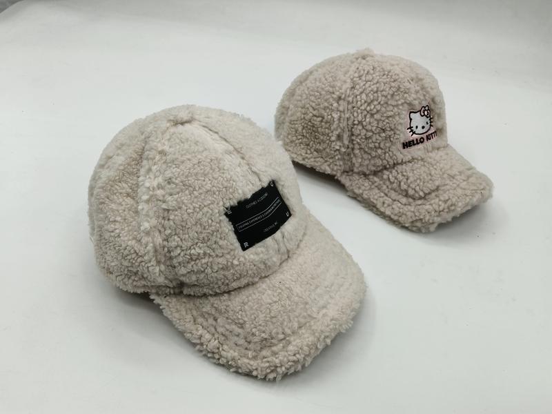 Två creme sherpa fleece-kepsar: en med svart etikettlapp och en med Hello Kitty-brodyr