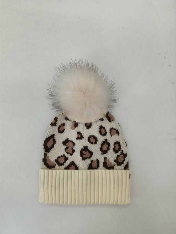 Krämvit stickad mössa med brunt leopardmönster och fluffig vit pompong i konstpäls