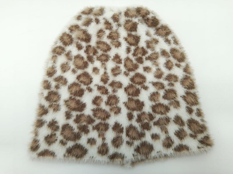 `Närbild på mjuk faux fur-tyg med brunt leopardmönster mot krämvit bakgrund.`