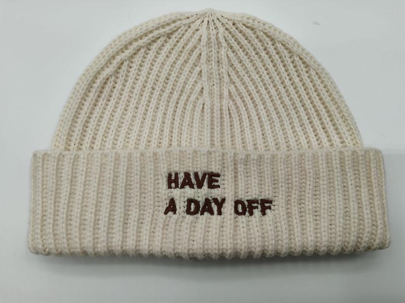 Crèmefärgad ribbstickad mössa med brunt broderat texten ""Have A Day Off"" på uppvikt kant.