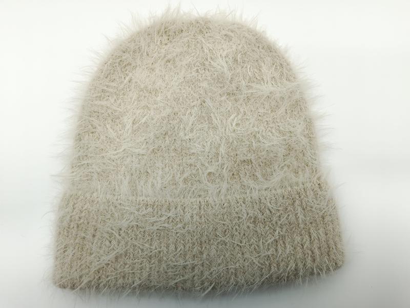 Cremefärgad fluffig ögonfranssstickad mössa med ribbad kant på vit bakgrund.