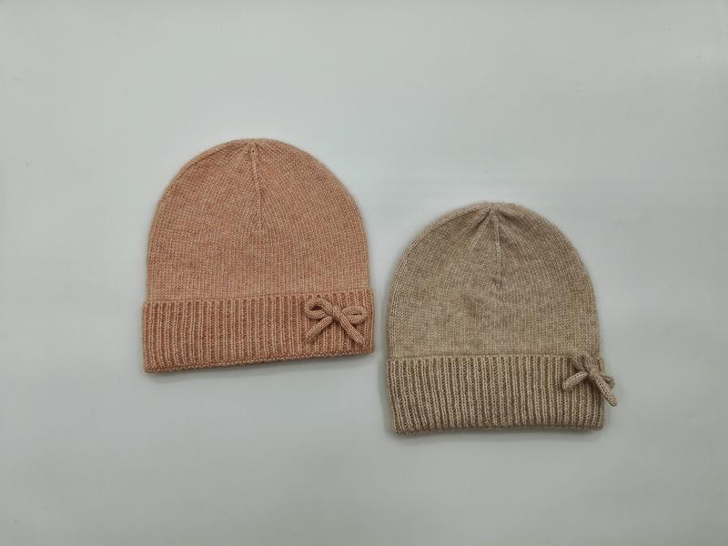 Två mjuka stickade mössor med ribbad uppvik och rosettdetalj i rosa och beige