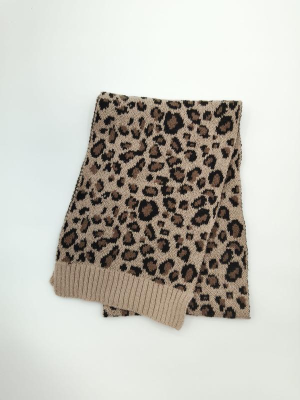 Veckad beige och svart stickad halsduk med leopardmönster och ribbade kanter på vit bakgrund.