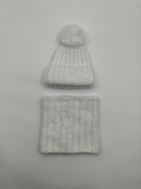 Vit fluffig ribbstickad vintermössa med pompom av konstpäls och matchande halsvärmare på grå bakgrund.