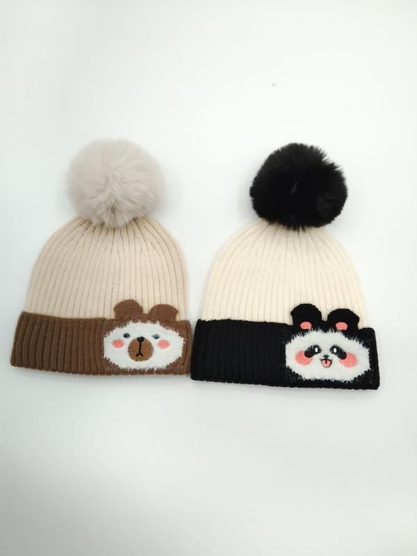 Två stickade mössor med pompom: brun björndesign på beige mössa och pandadesign på svart och vit mössa.