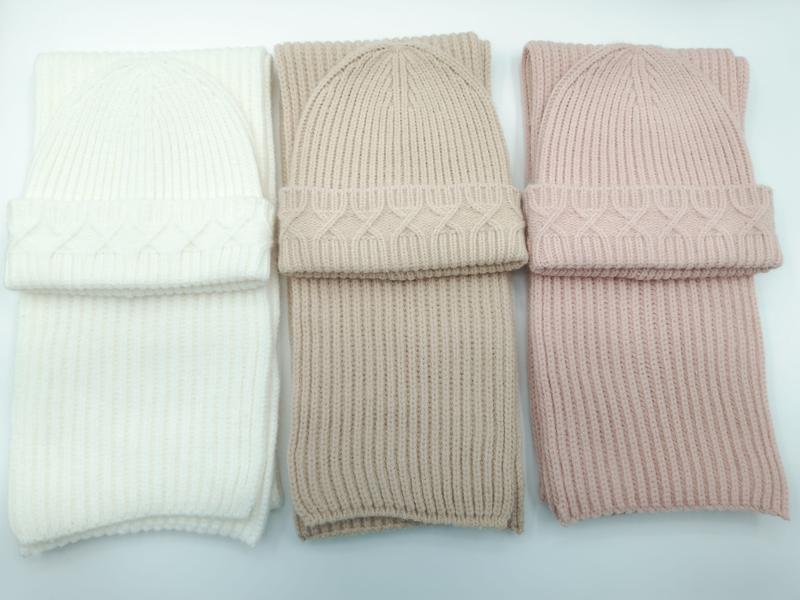 Tre matchande set med kabelstickad mössa och ribbad halsduk i vitt, taupe och pudderrosa på vit bakgrund.