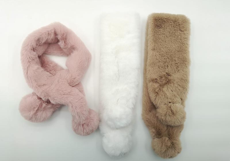 Tre fluffiga konstpälssjalar i rosa, vit och beige med pompomändar, liggande på vit bakgrund.