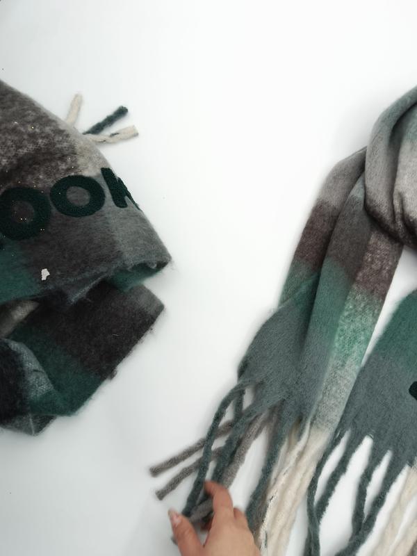 Grön, grå och brun rutig ullblandningsscarf med fransar, en vikt och en utvikt på vit yta.