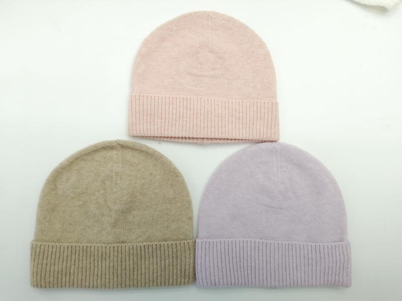 Tre stickade mössor i rosa, taupe och lavendel med ribbade uppvik, fotograferade uppifrån mot vit bakgrund.